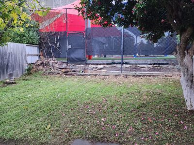 Tidied backyard in Brighton with mowed grass, brick paving, a large flowering tree, and a cleared fence line beside a chain-link fence.